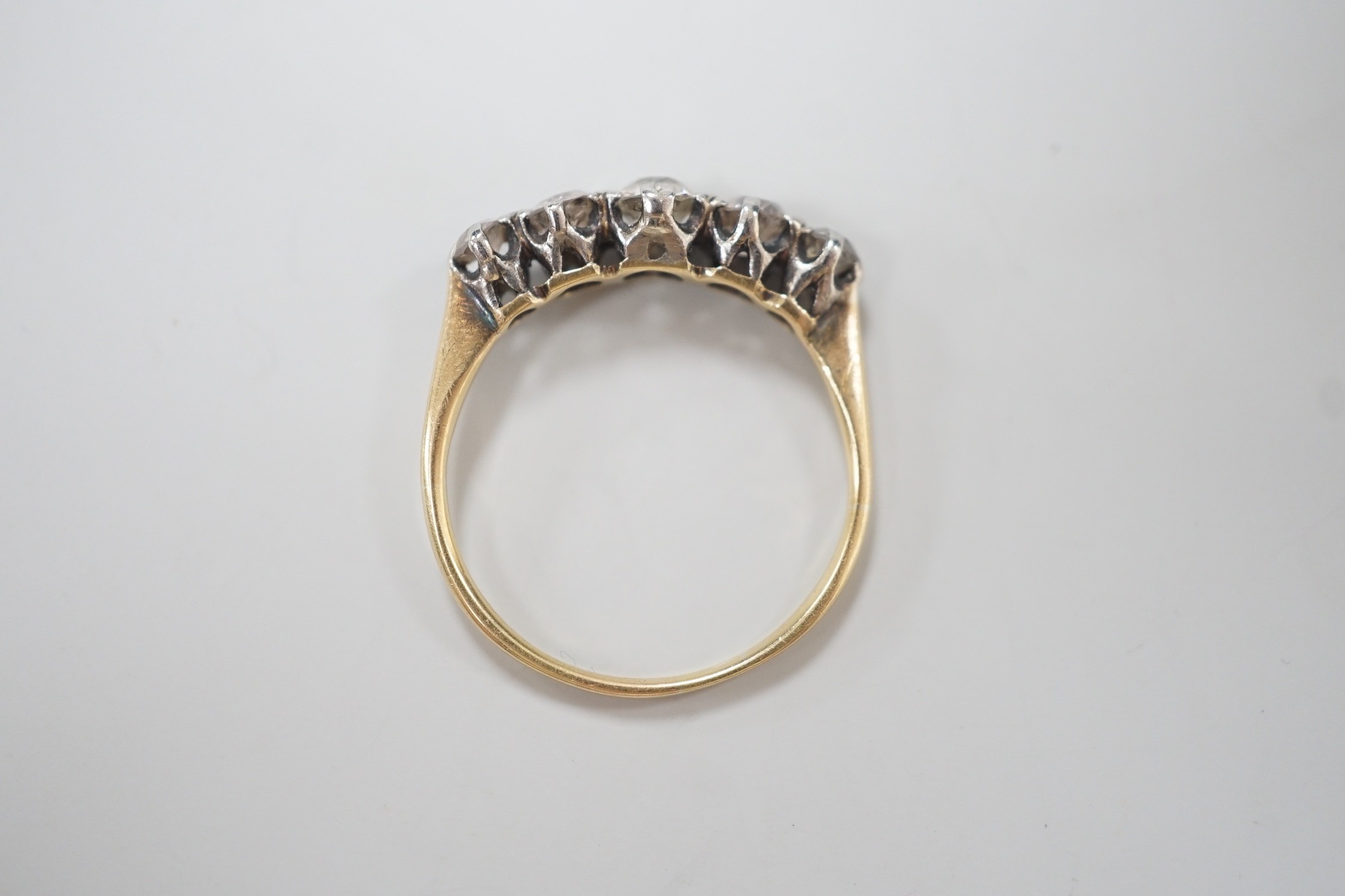 A yellow metal and graduated five stone diamond set half hoop ring, size O, gross weight 2.3 grams.